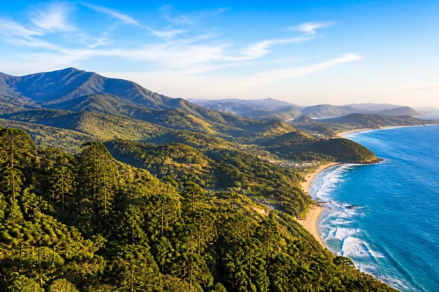 Vista panorâmica mostrando as montanhas verdes de Campos do Jordão ao lado da costa com praias e mar azul de Ubatuba.