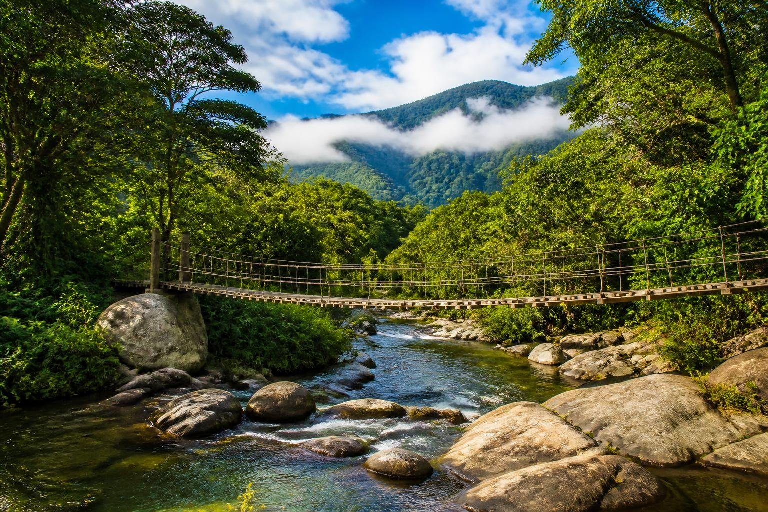 Paisagem natural de Visconde de Mauá com montanhas verdes, rio cristalino e uma ponte suspensa de madeira.