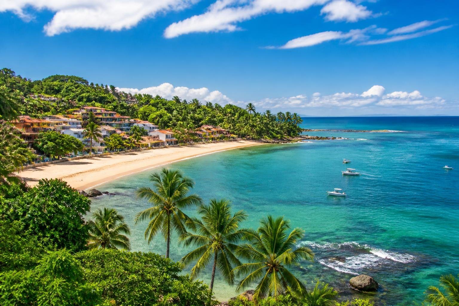 Vista panorâmica da costa de Morro de São Paulo com praias de areia dourada, águas turquesa, vegetação tropical e casas coloridas na encosta.
