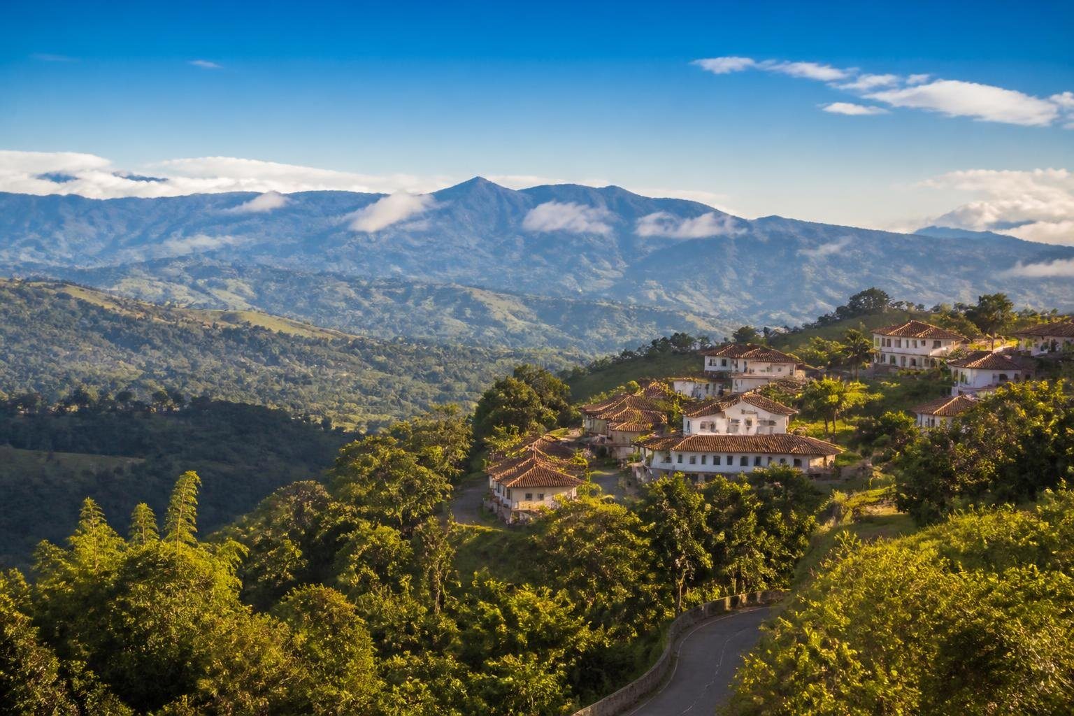 Vista panorâmica das cidades da Serra da Mantiqueira com montanhas verdes, casas coloniais e céu azul claro.