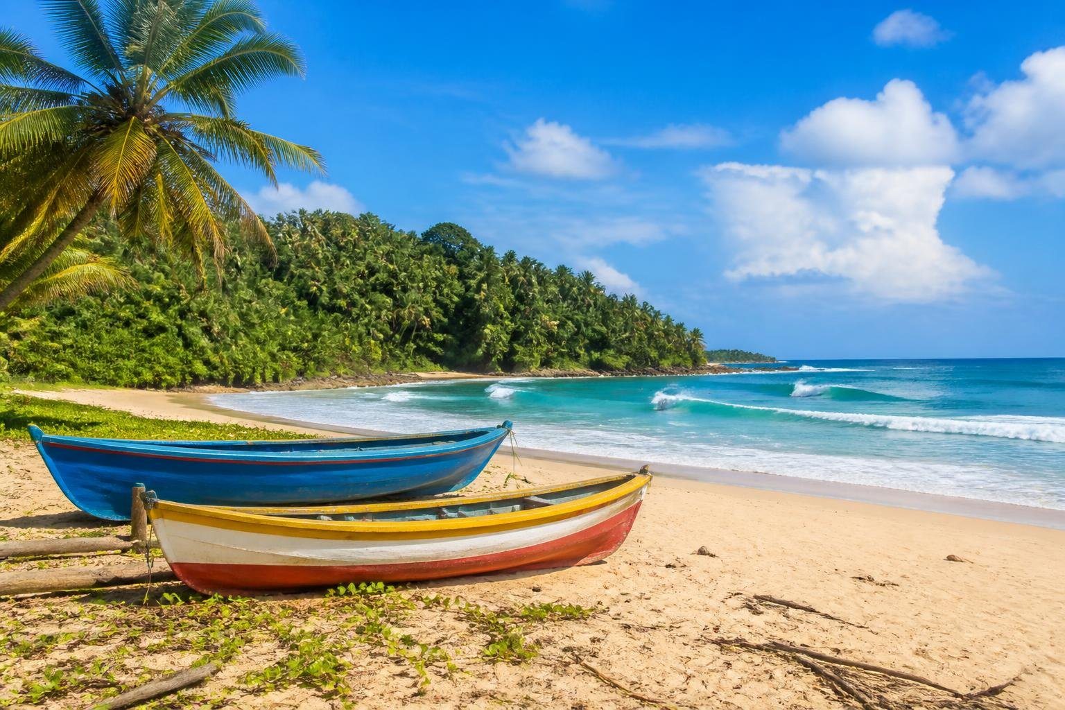 Praia tropical em Itacaré com areia dourada, palmeiras verdes, ondas azuis e barcos de pesca coloridos na areia.